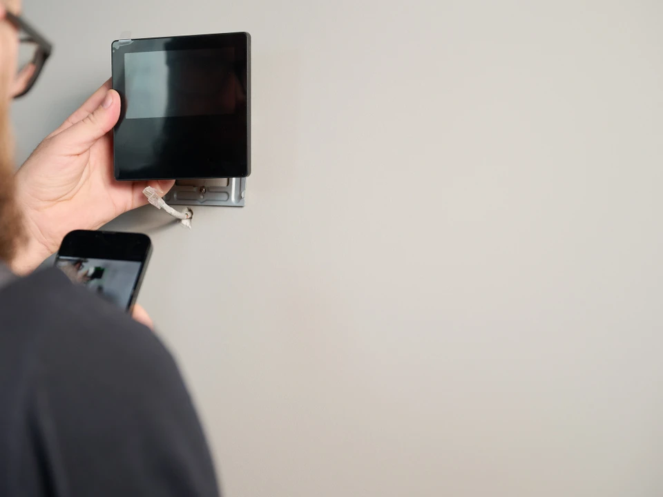 Un électricien travaille dans un tableau électrique ouvert, manipulant des fils avec un outil de précision