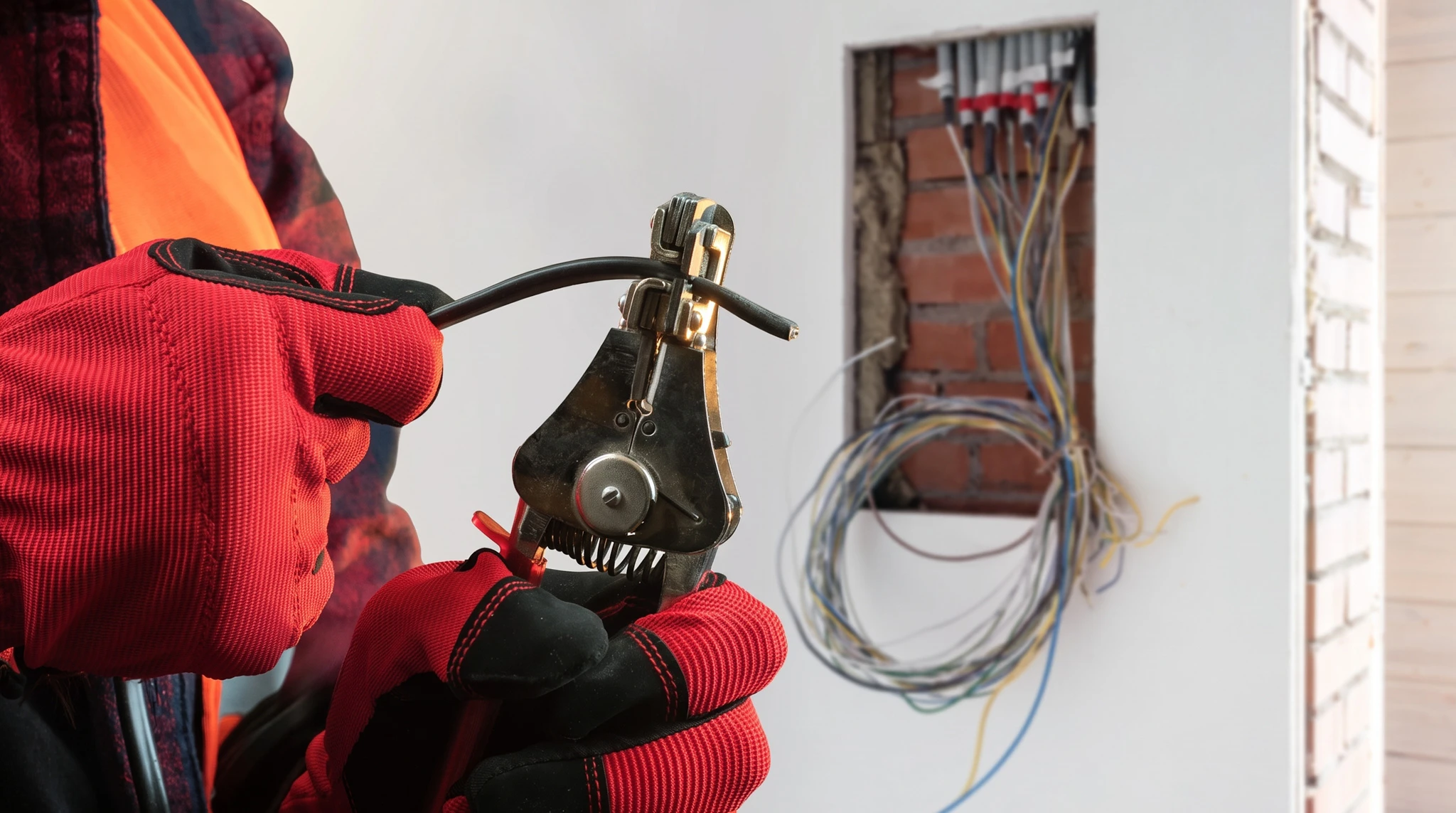 Électricien en combinaison bleue installant une prise électrique murale dans un intérieur résidentiel blanc